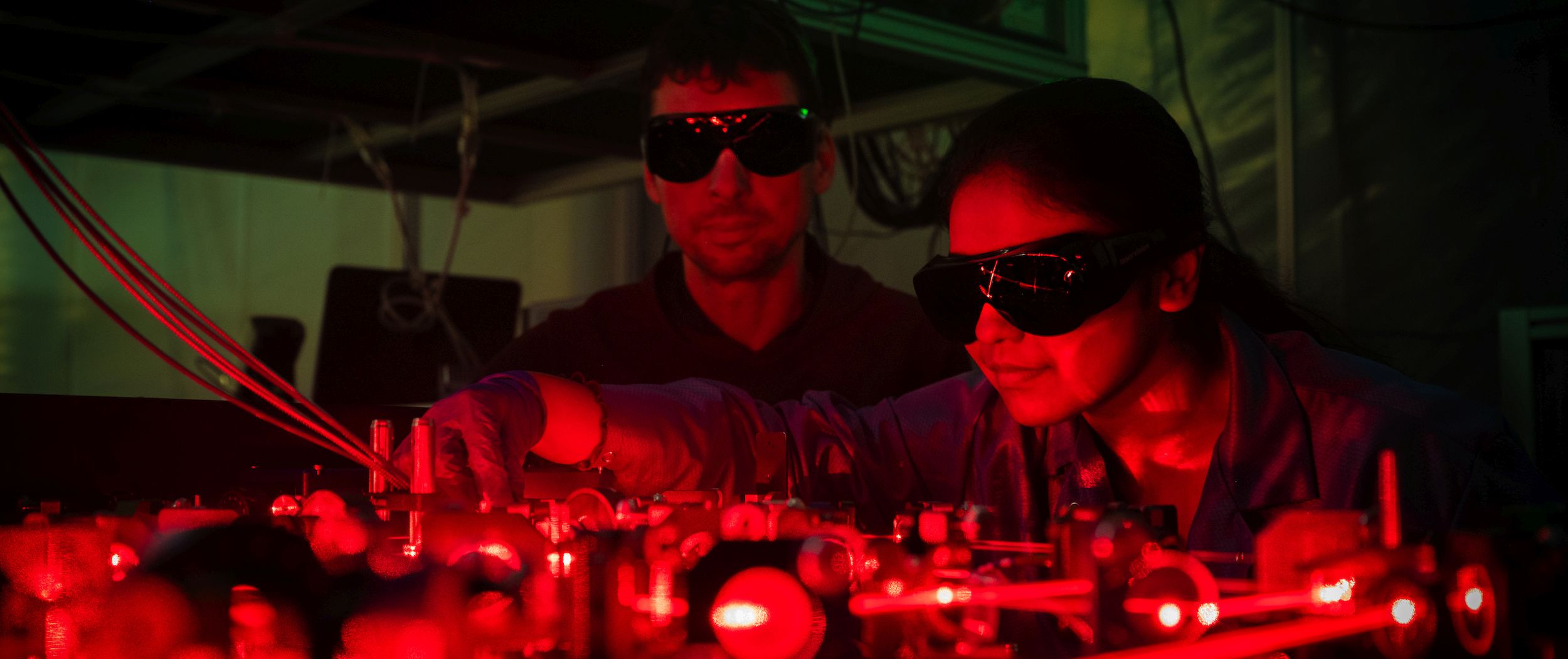 Two persons working in the red glow of the laser lab